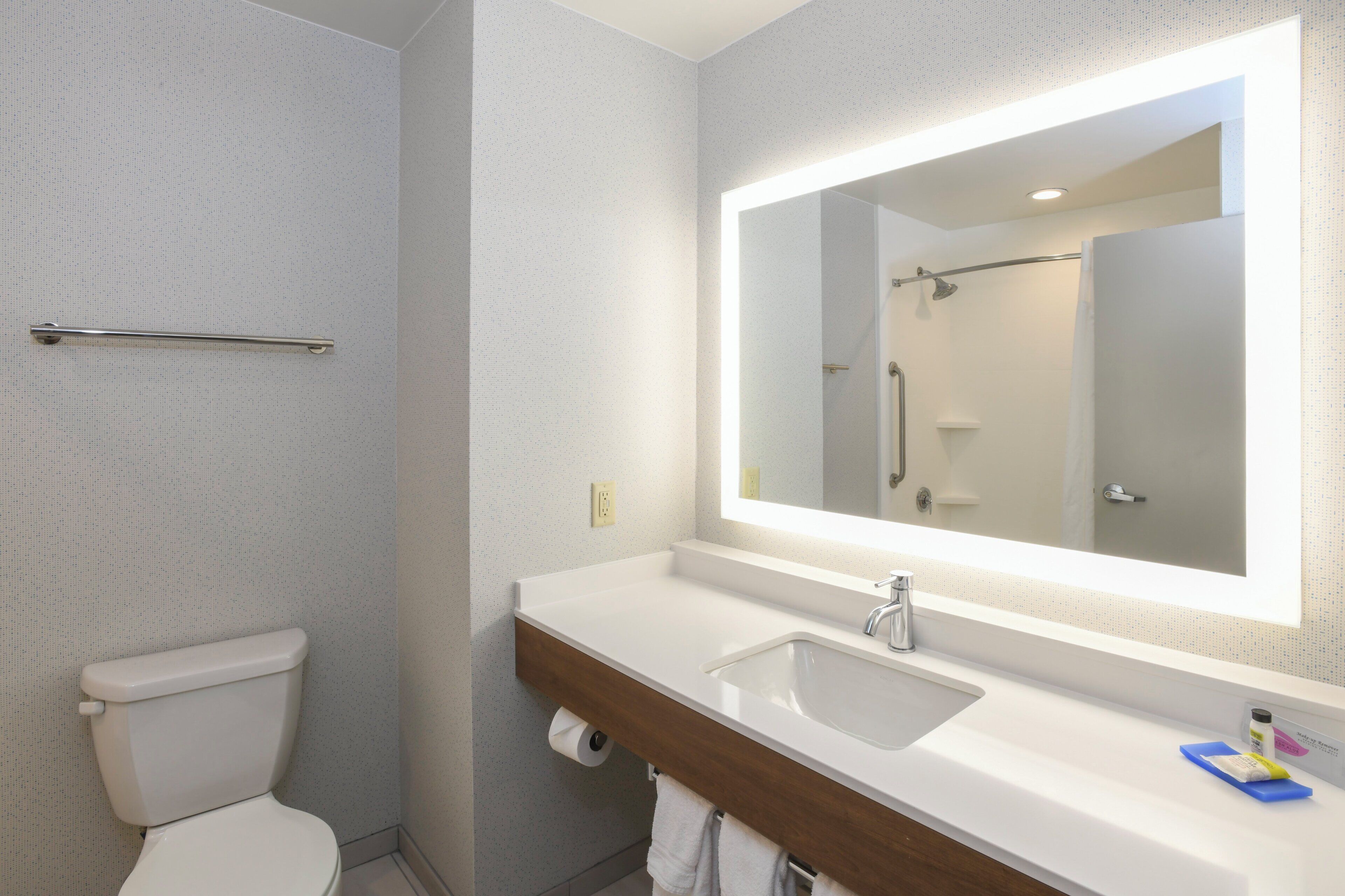 Un baño con inodoro blanco, lavamanos con espejo y zona de ducha.