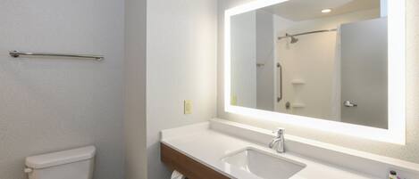 Un baño con inodoro blanco, lavamanos con espejo y zona de ducha.