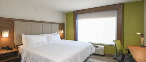 Habitación de hotel con una cama grande, un escritorio, una silla, una mesita de noche y un ventanal con persianas.
