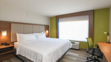 Une chambre d’hôtel avec un lit, une table de chevet, une lampe, une chaise et une fenêtre.
