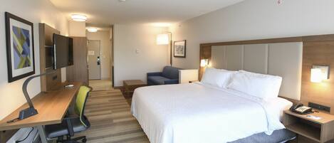 A hotel room with a large bed, a desk with a chair, a television, and a bedside table with a lamp.