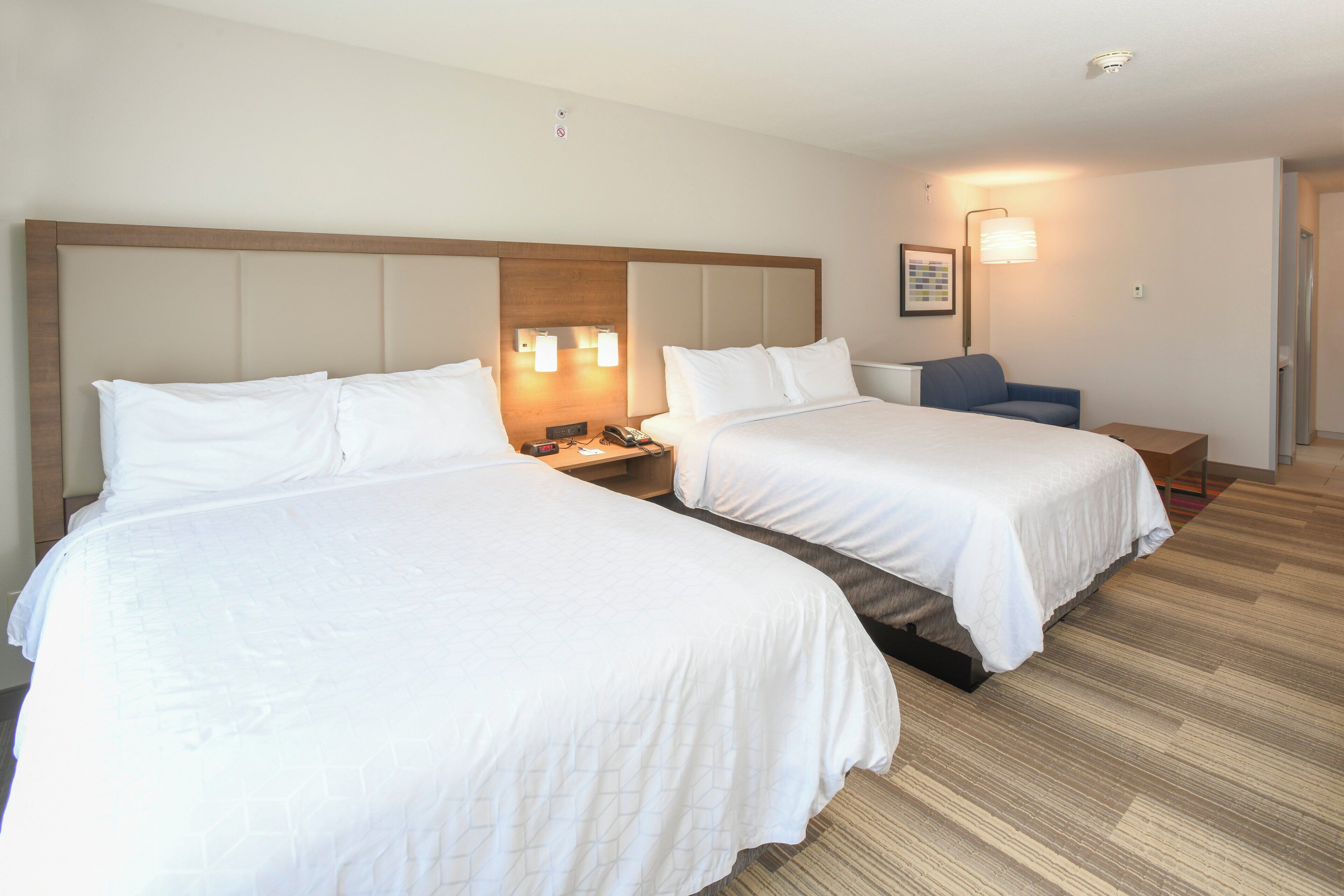 A hotel room with two beds, a desk, a chair, and a nightstand with a phone.
