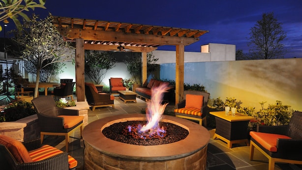 An outdoor patio area with a stone fire pit, wicker furniture, and a wooden pergola. - Houston Marriott Energy Corridor (Houston)