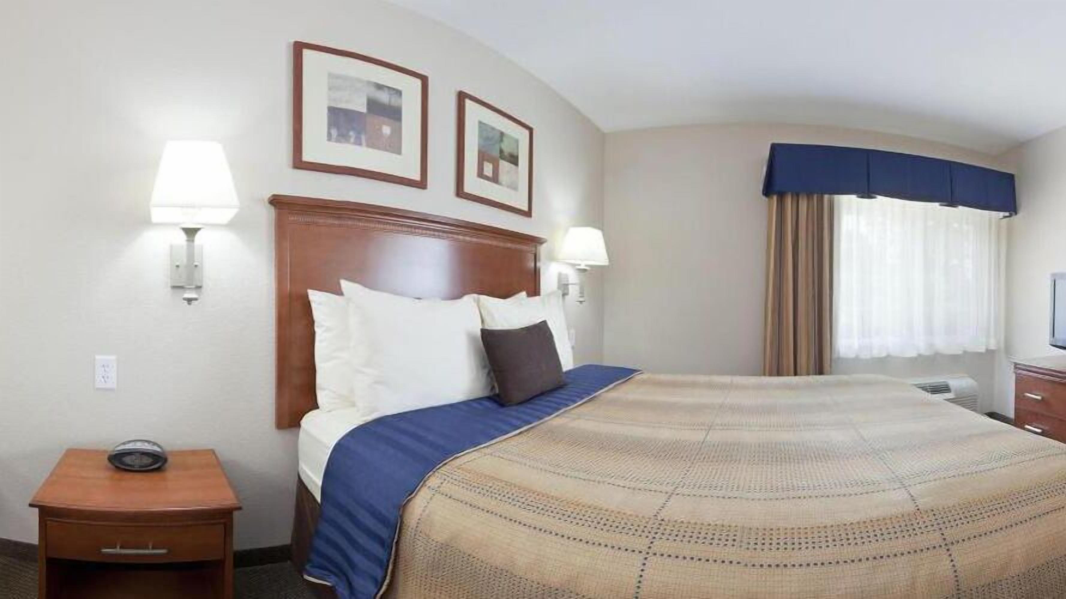 Une chambre d’hôtel avec un grand lit, deux lampes fixées au mur, une table de chevet avec un téléphone et une fenêtre avec des rideaux.