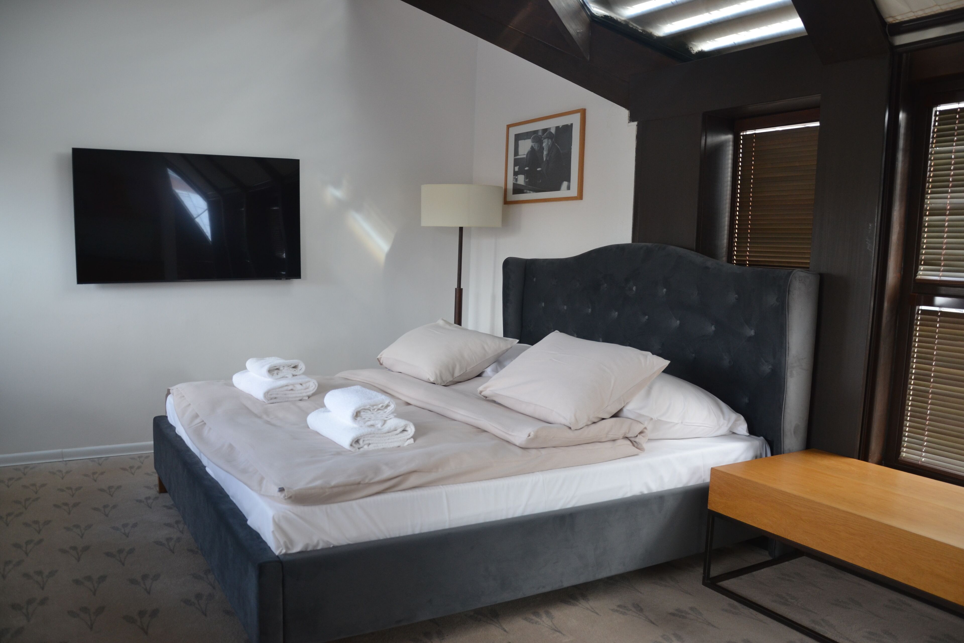 A neatly made bed with towels, a bedside table, a lamp, and a television on the wall.