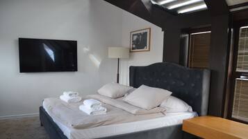 A neatly made bed with towels, a bedside table, a lamp, and a television on the wall.