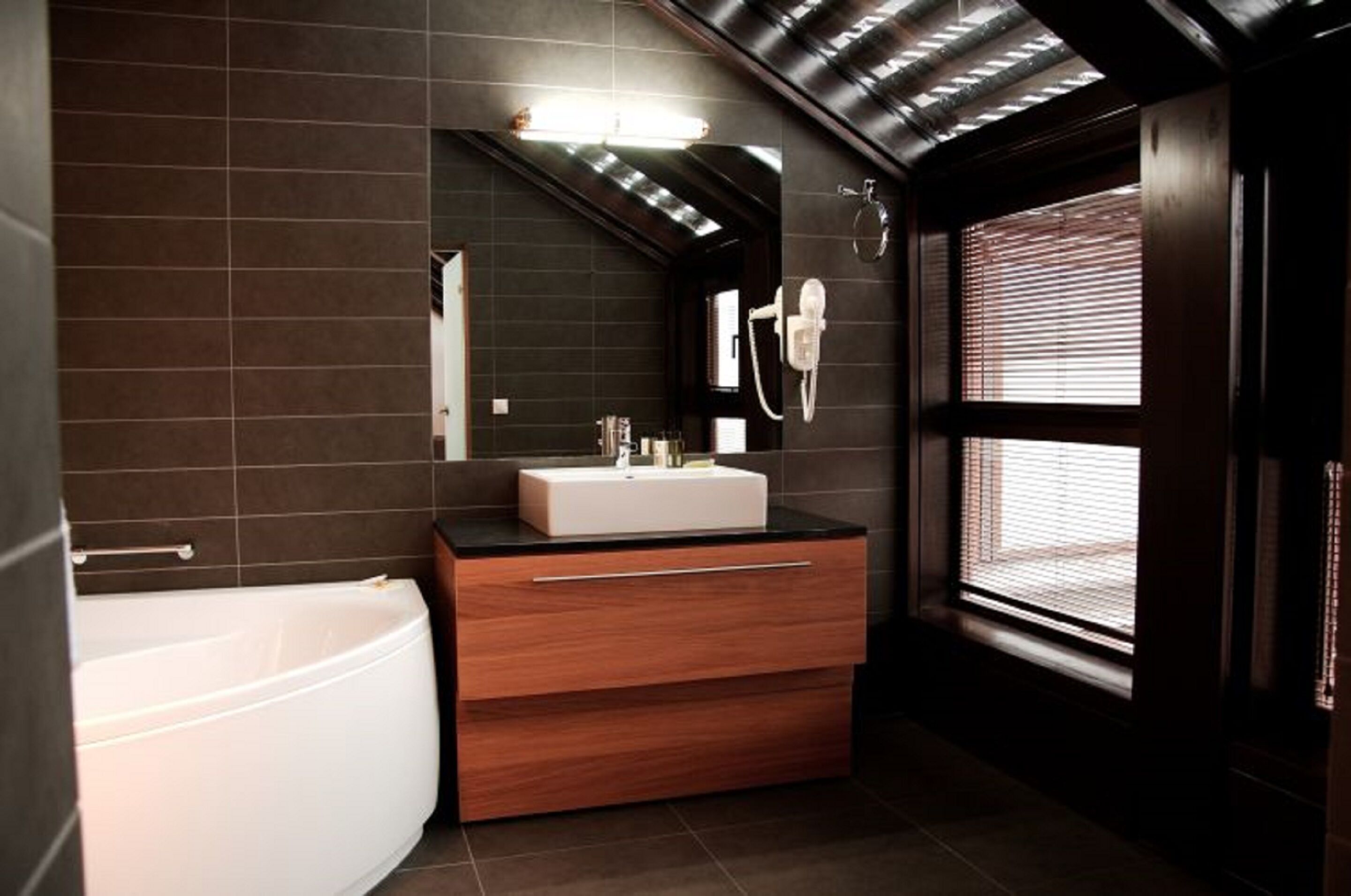 Ein modernes Badezimmer mit einer freistehenden Badewanne, einem Waschtisch mit Spiegel und einem Fenster mit Jalousien.