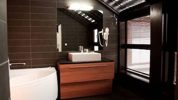 Ein modernes Badezimmer mit einer freistehenden Badewanne, einem Waschtisch mit Spiegel und einem Fenster mit Jalousien.