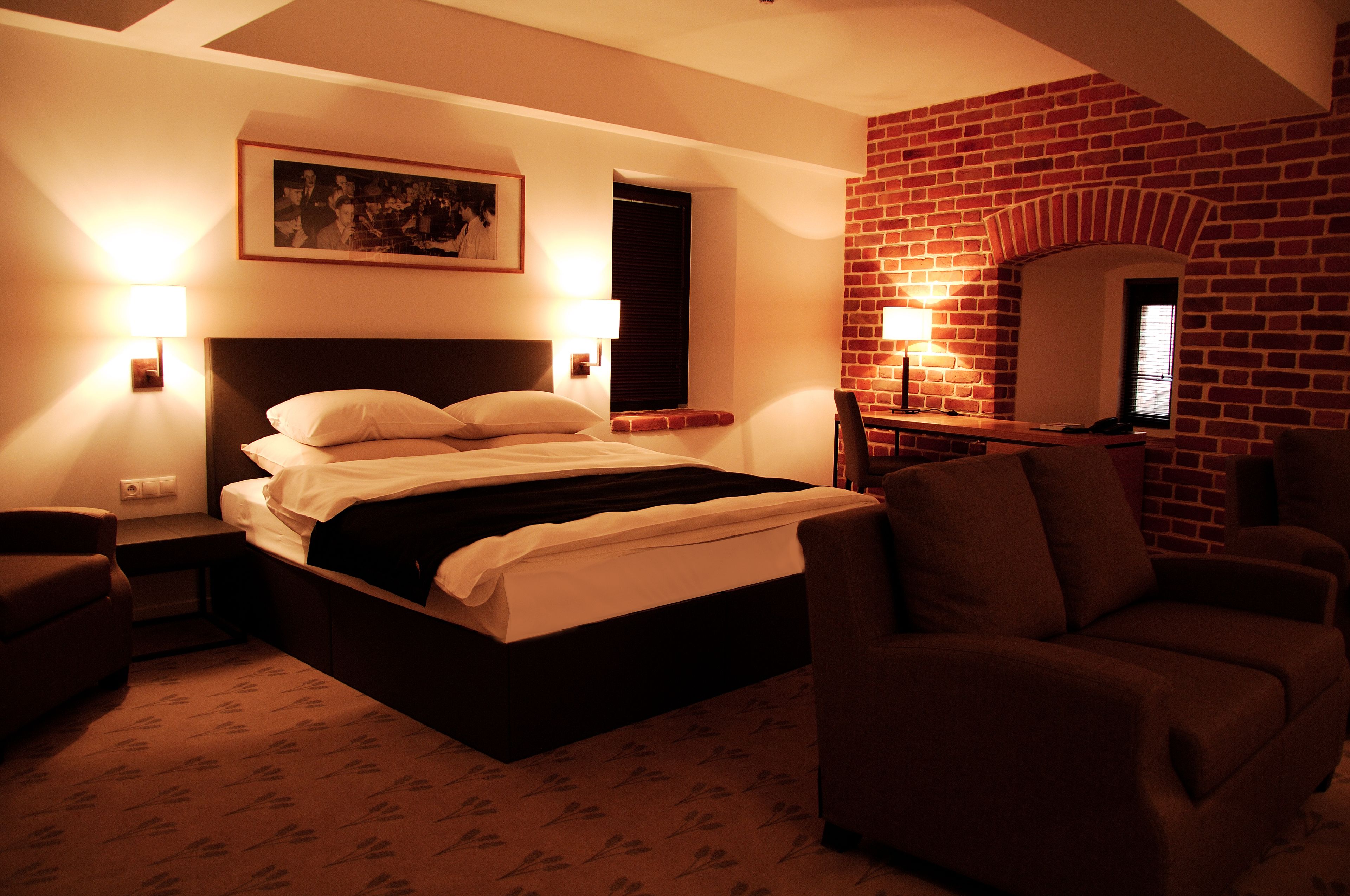 Habitación de hotel con una cama grande, dos lámparas de noche, una pared de ladrillo y un cuadro enmarcado.