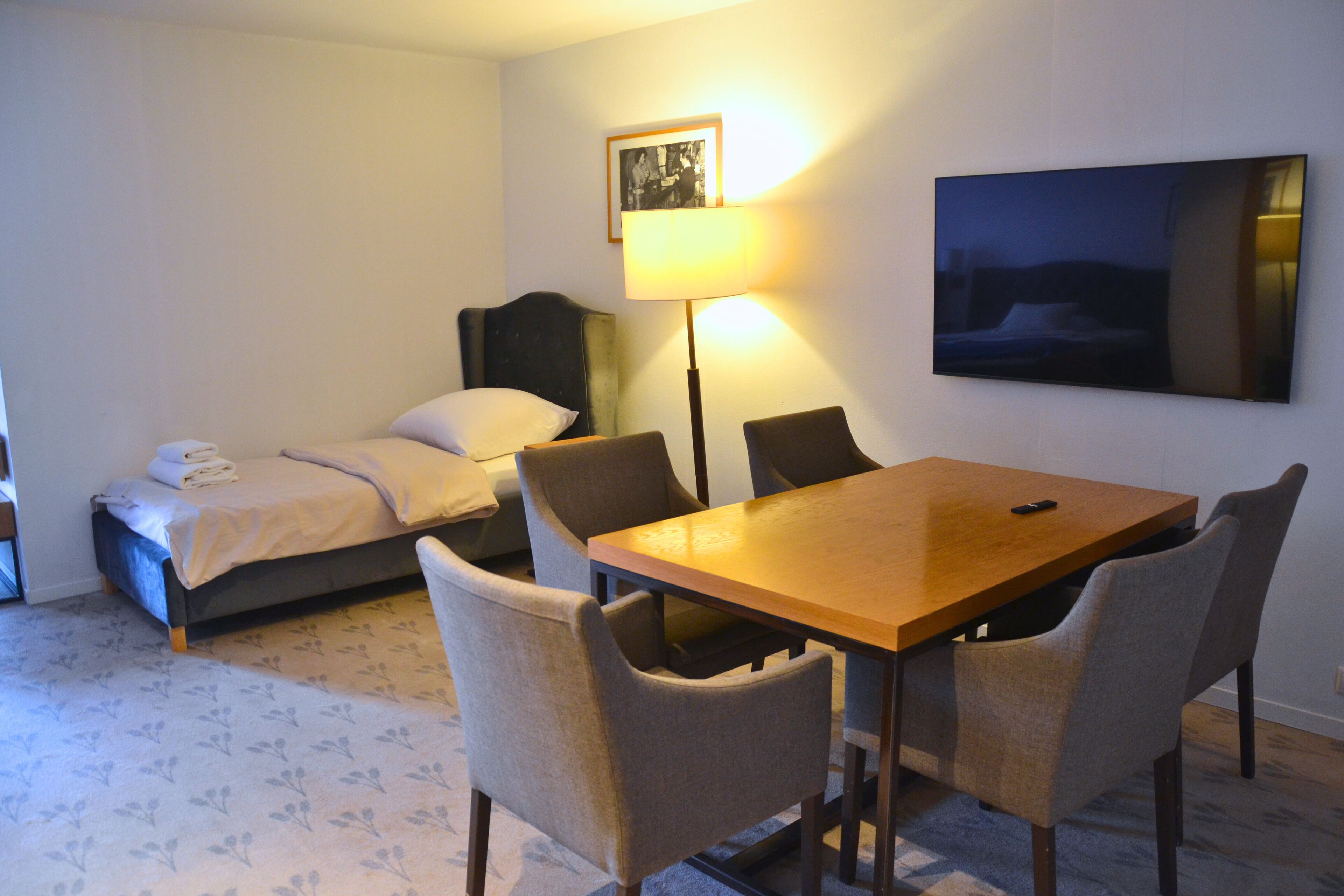 Habitación de hotel con cama, una mesa con sillas, una lámpara y un cuadro en la pared.
