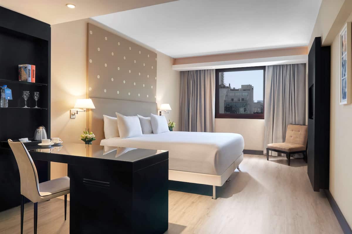 Une chambre d’hôtel avec un lit, un bureau, une chaise et une vue sur la ville.