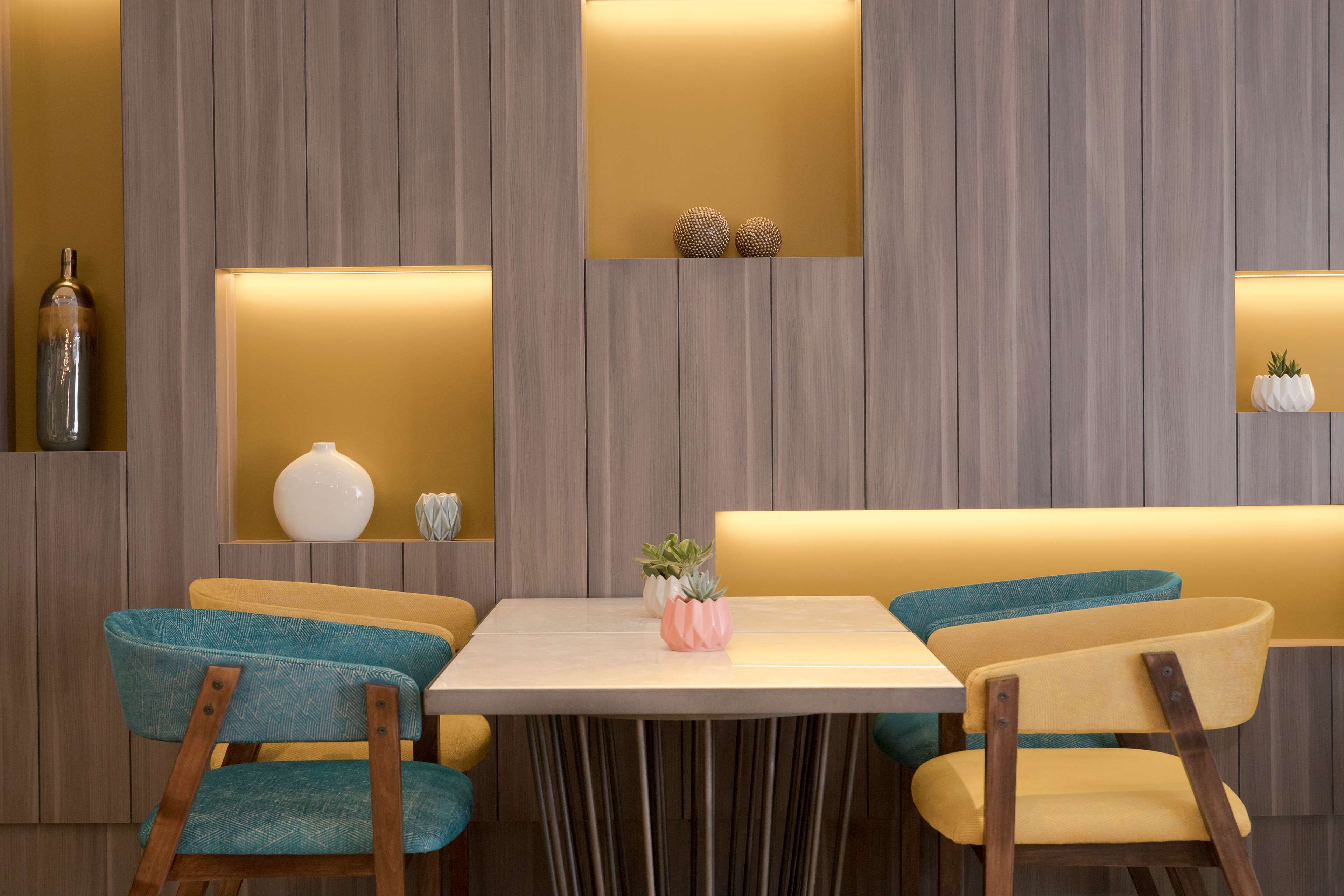 Un comedor moderno con una pared de madera, una mesa y dos sillas con tapicería verde aguamarina y amarilla.
