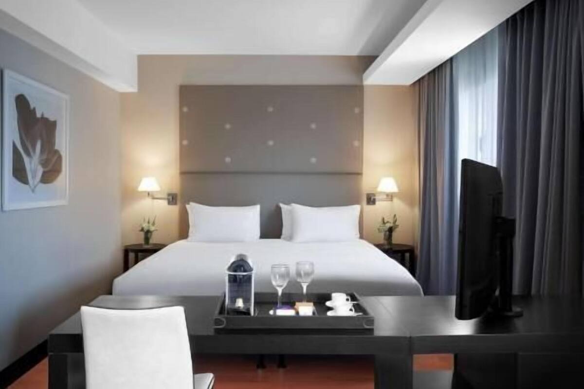 Une chambre d’hôtel comprenant un lit, deux lampes de chevet, un téléviseur à écran plat, un bureau avec un plateau et une chaise.
