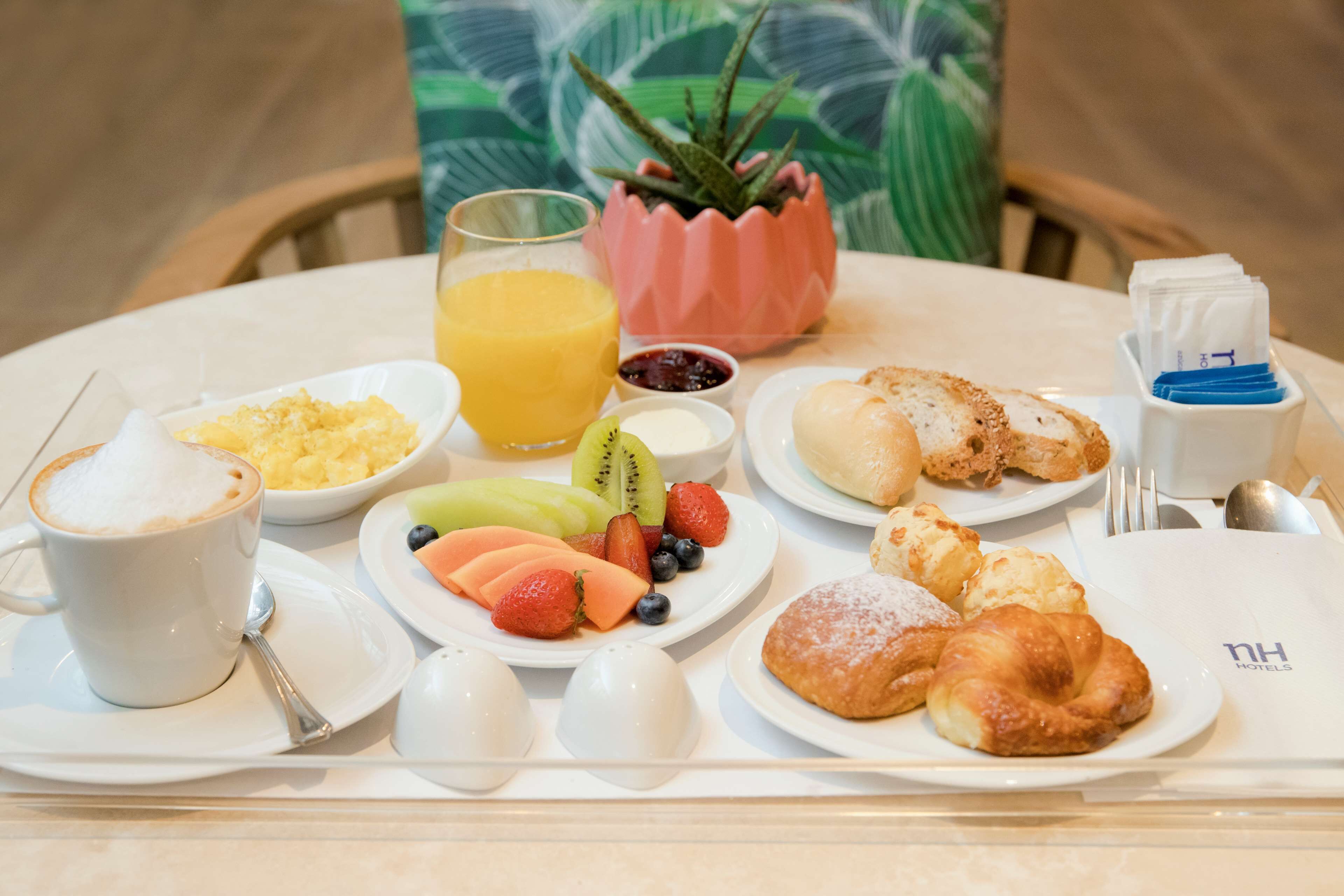 A breakfast tray with a cup of coffee, a glass of orange juice, a bowl of fruit, croissants, and a pastry.
