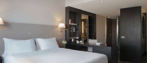 Una habitación de hotel moderna con una cama grande, lámparas de noche, un escritorio integrado y un piso de madera oscura.