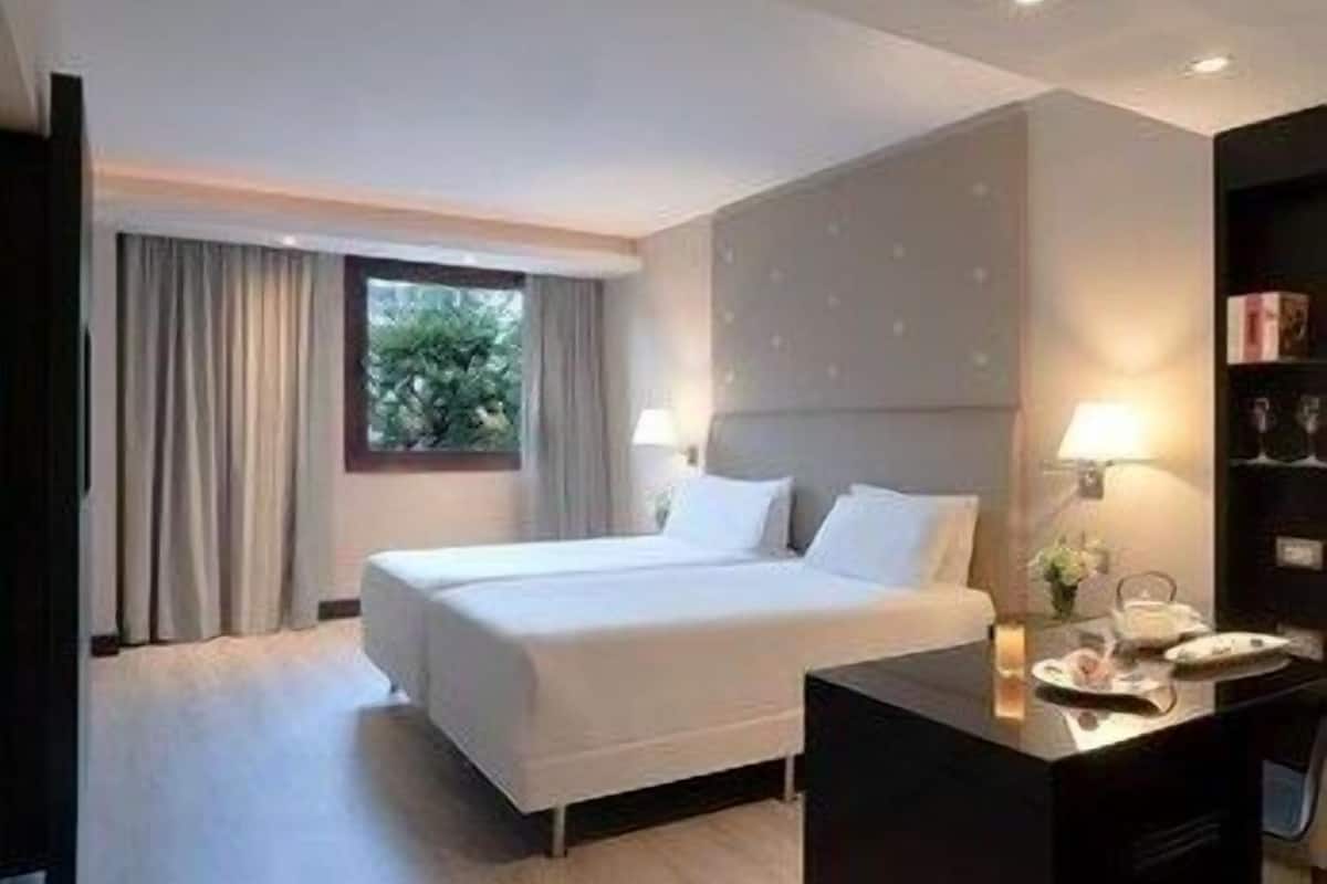 Une chambre d’hôtel avec un grand lit, un bureau avec une lampe et une vue sur la verdure.