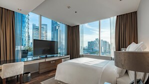 A modern hotel room with a large bed, a desk with a flat-screen TV, a chair, and a view of the cityscape through large windows. - MUU Bangkok, Small Luxury Hotels of the World (Bangkok)