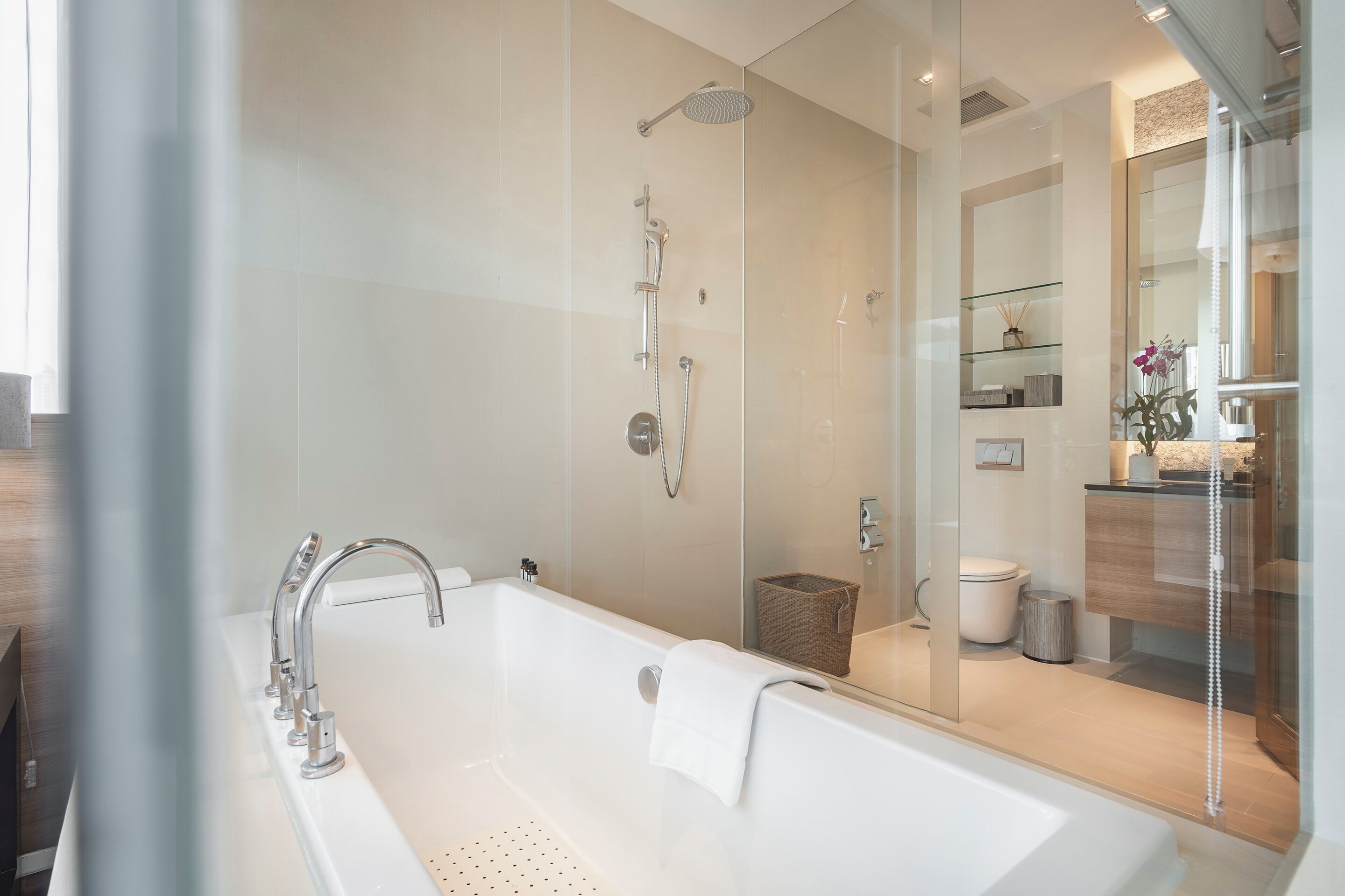 Une salle de bain moderne dotée d’une grande baignoire, d’une douche séparée par une paroi de verre et de toilettes apparentes.