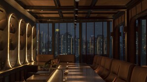 A modern bar with a long counter, leather seating, and large windows offering a city view. - MUU Bangkok, Small Luxury Hotels of the World (Bangkok)
