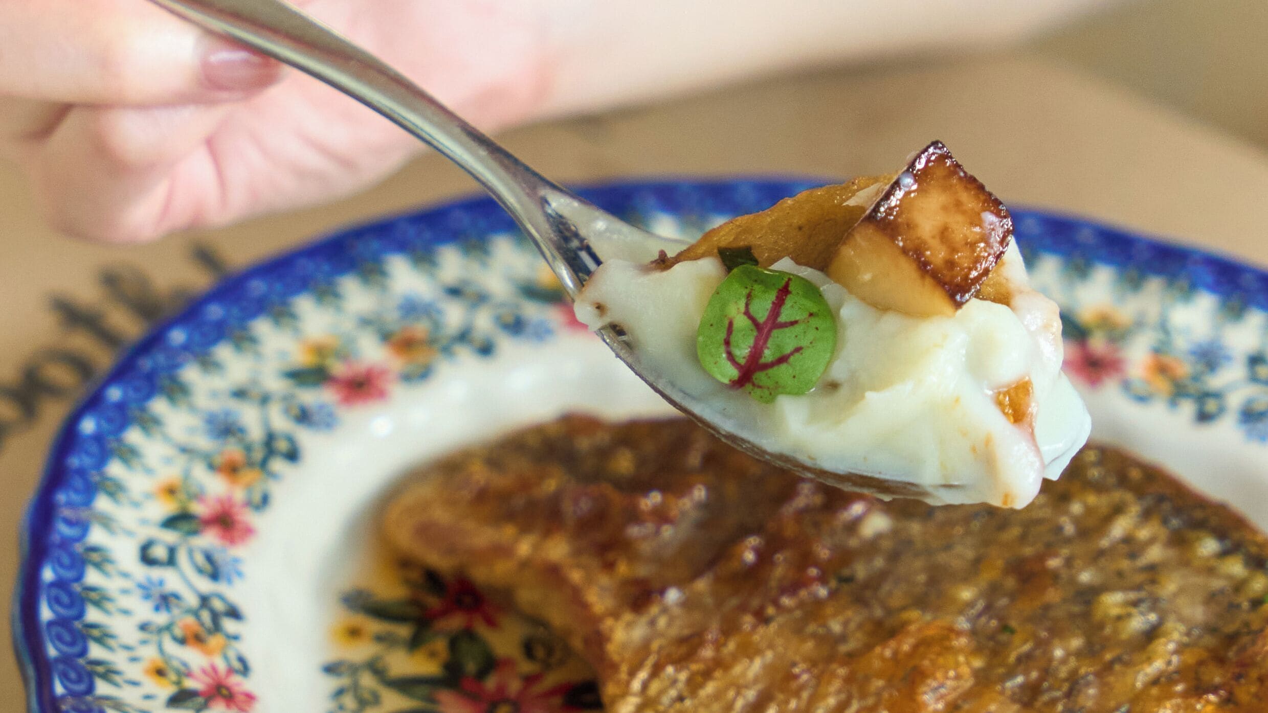 A spoonful of food with a green leaf garnish on a floral plate.
