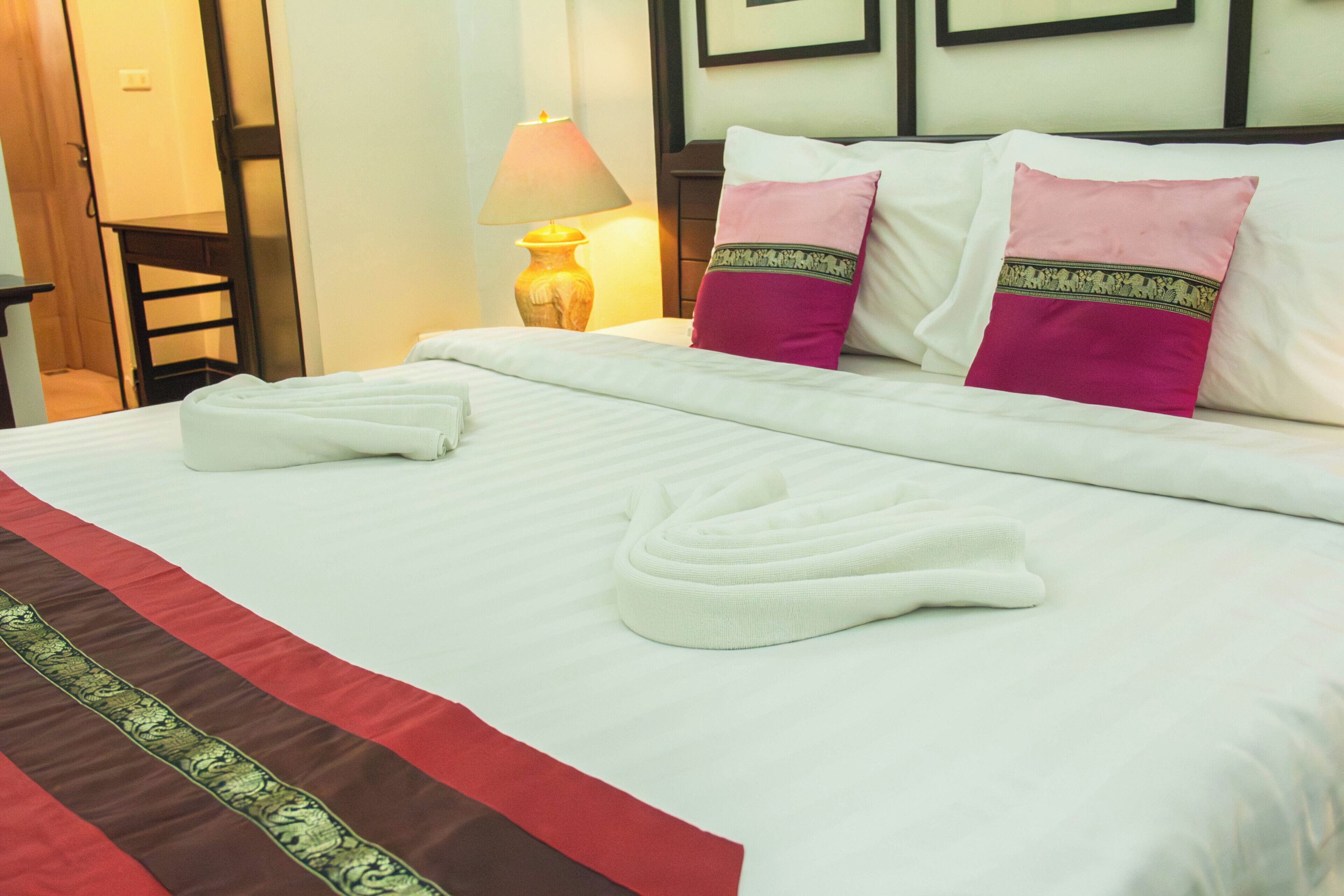 A neatly made bed with white linens, two pillows with decorative borders, and a pair of folded towels.