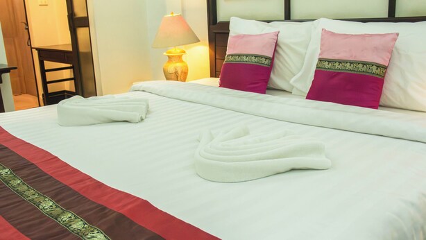 A neatly made bed with white linens, two pillows with decorative borders, and a pair of folded towels. - Sunday Rainforest Chiangmai Hotel  (Chiang Mai)