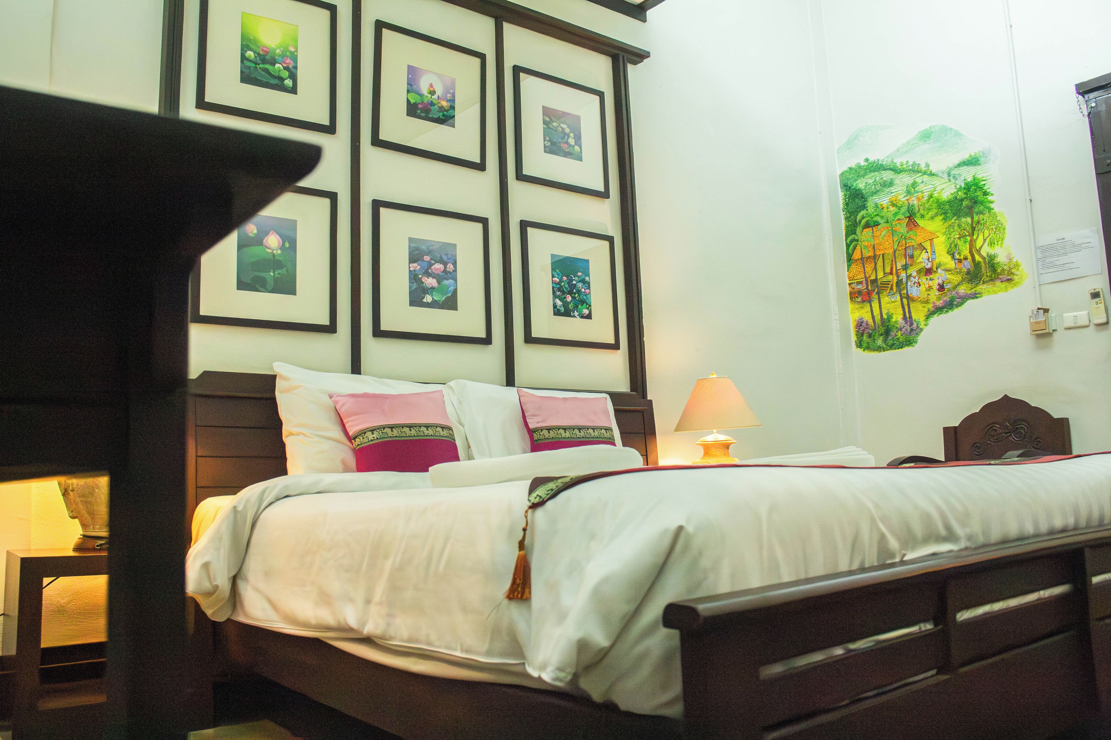 A hotel room with a bed, a nightstand, a lamp, and a wall with framed pictures.