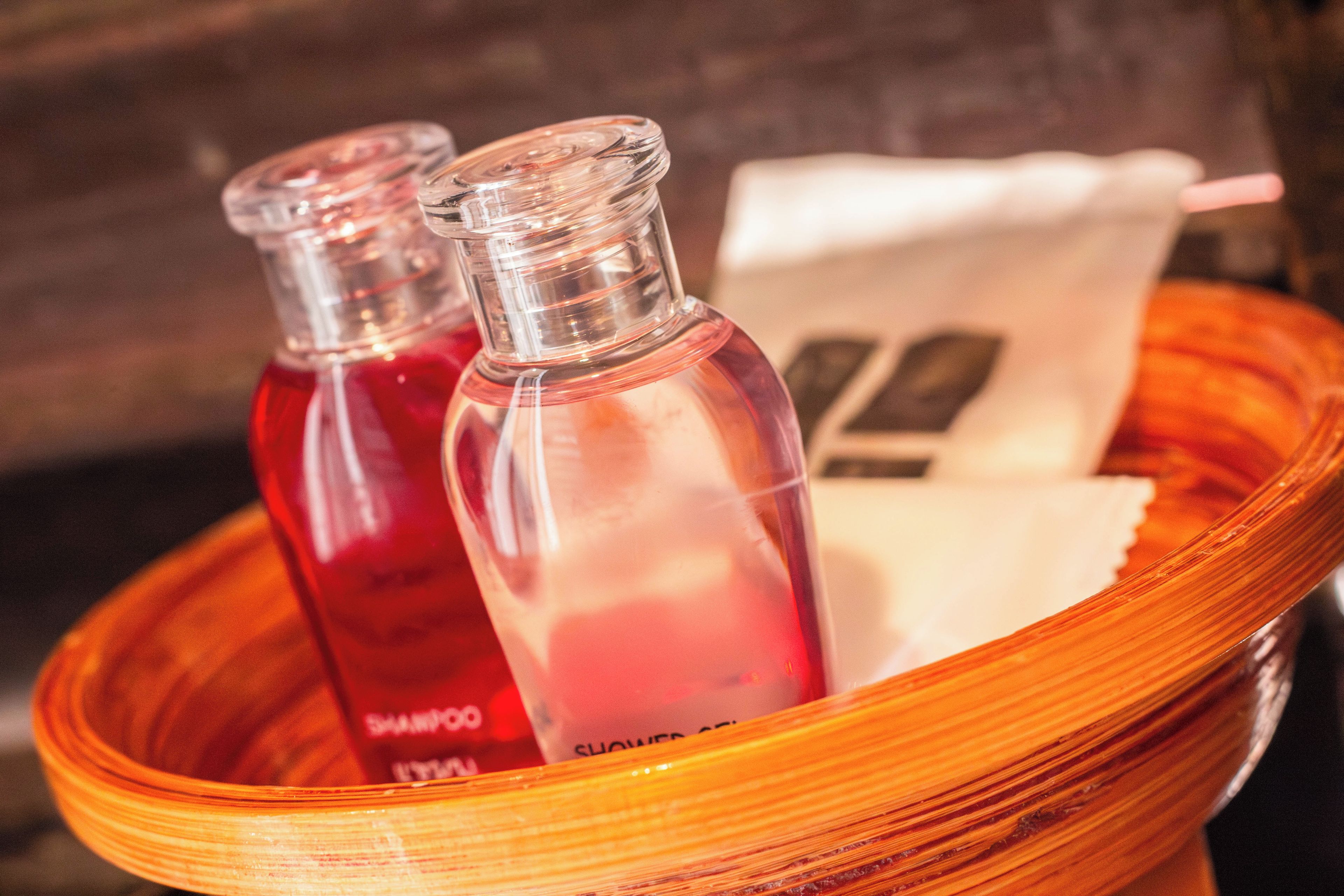 Two clear glass bottles with red liquid, possibly shampoo, in a wooden basket.