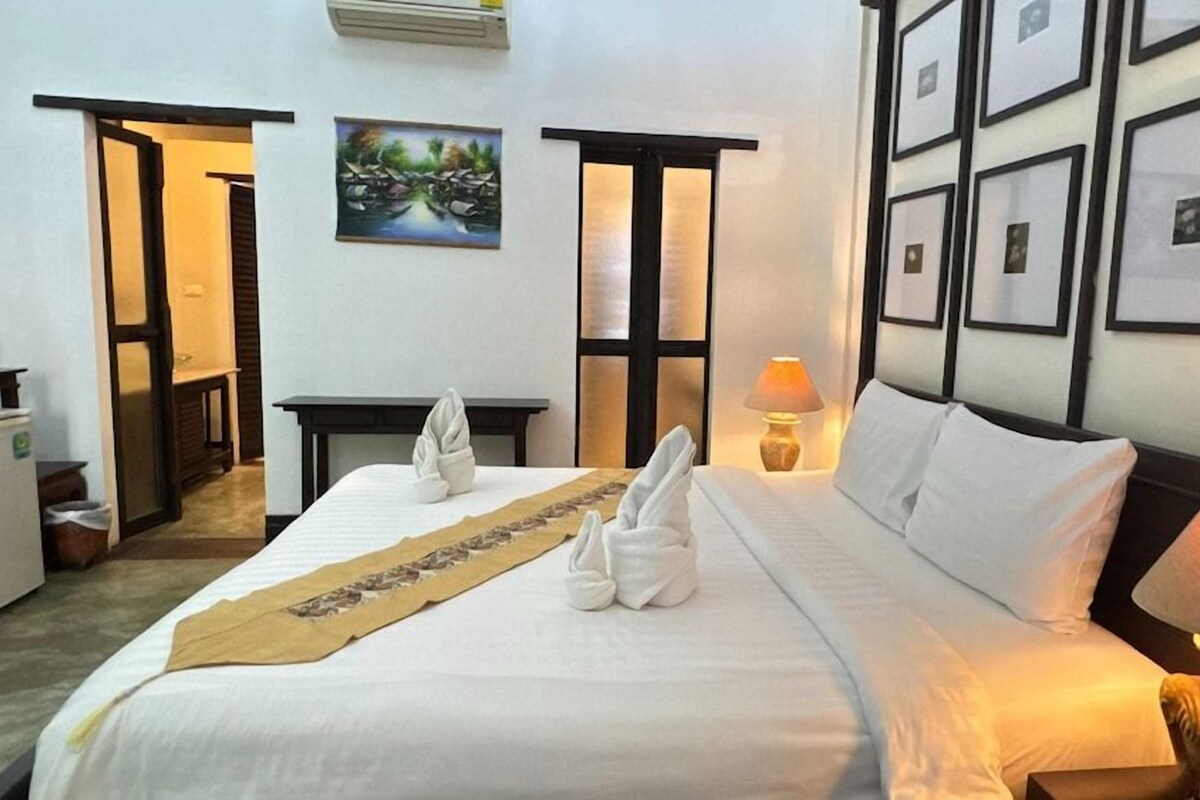 A hotel room with a bed, a bedside lamp, a picture frame, and a door leading to another room.