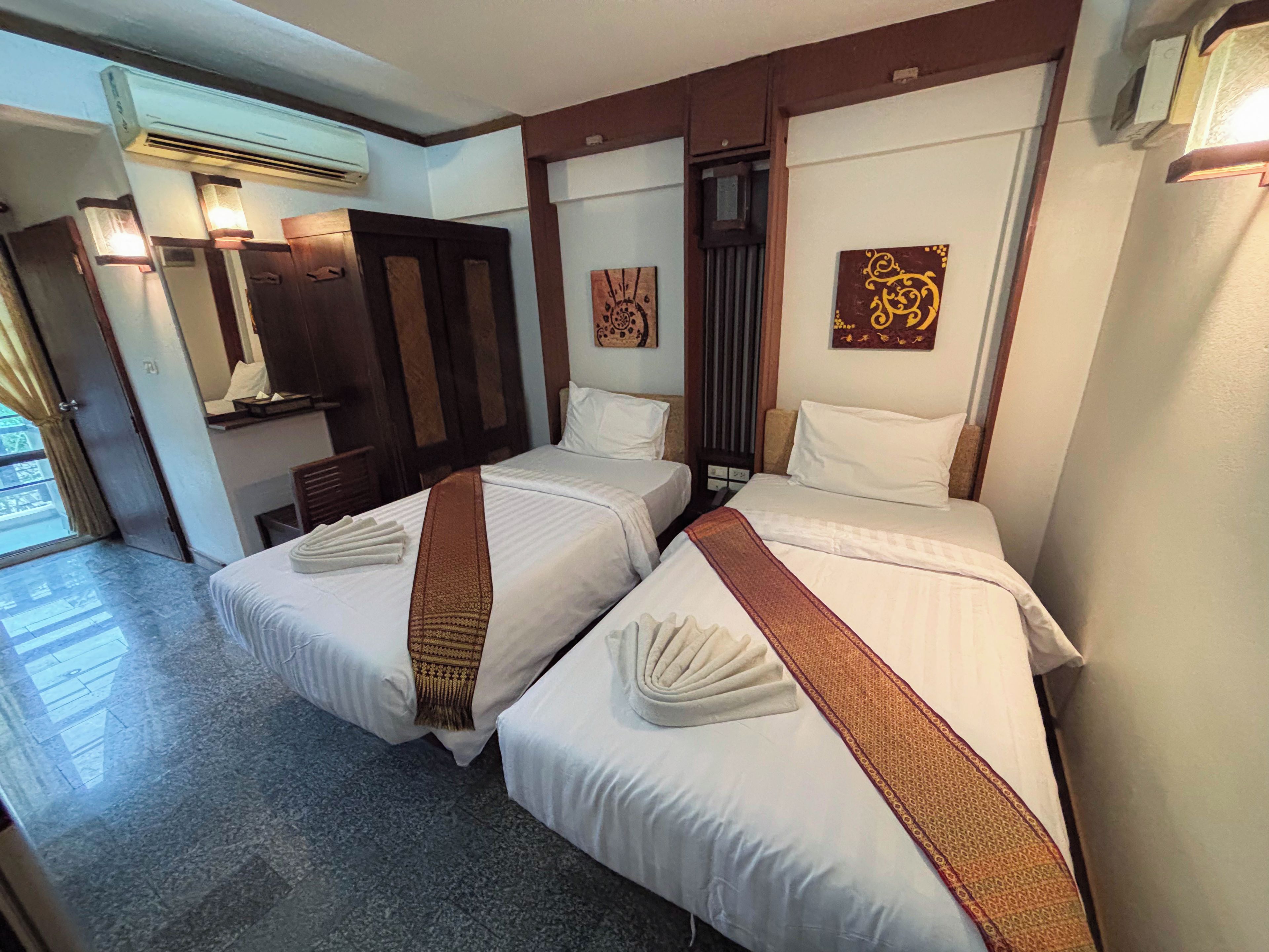 A hotel room with two beds, a mirror, a door, and a wall-mounted air conditioner.