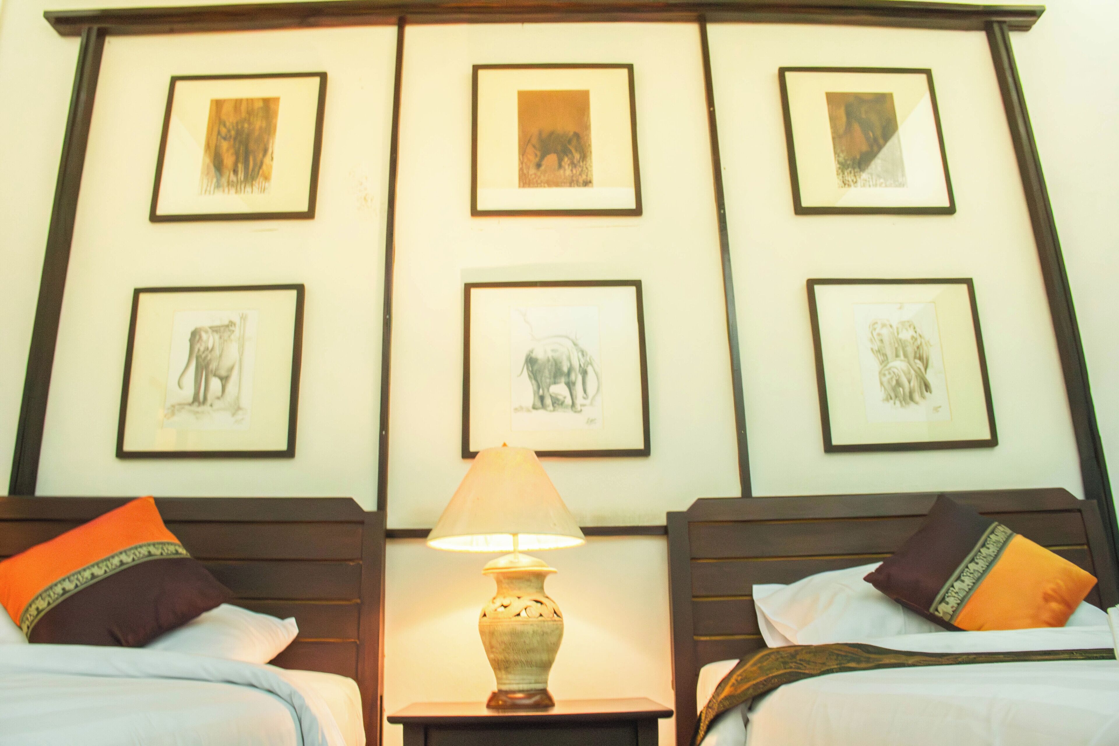 Une chambre d’hôtel avec deux lits, une table de chevet avec une lampe et des œuvres d’art encadrées accrochées au mur.