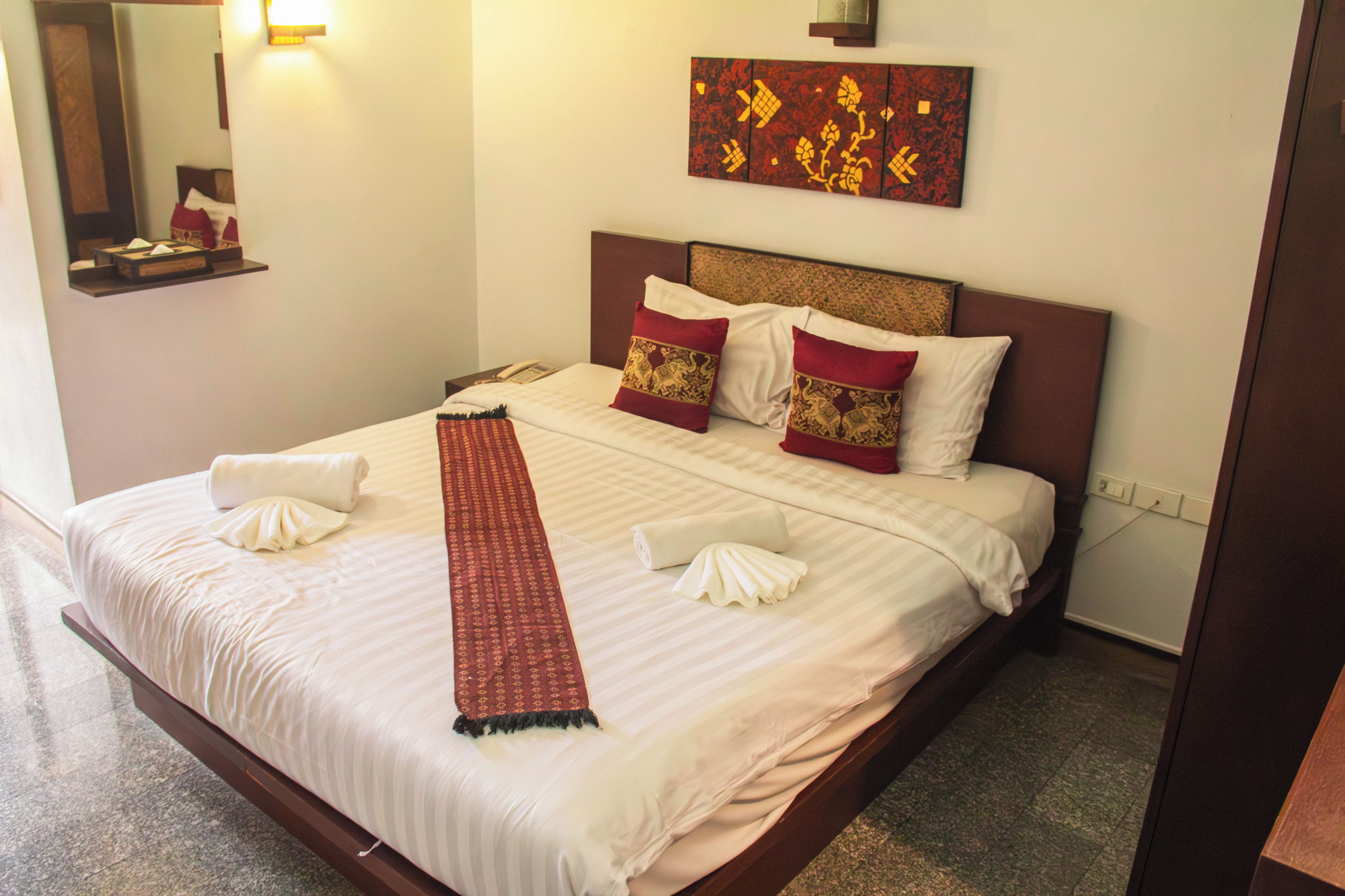A hotel room with a neatly made bed, a bedside table with a lamp, and a painting on the wall.