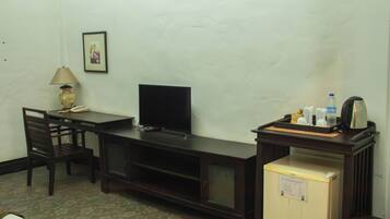 Quarto de hotel compacto com escrivaninha, televisão, pequena geladeira e cafeteira.