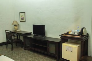 Habitación de hotel compacta con escritorio, televisión, refrigerador pequeño y cafetera.