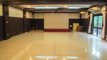 A spacious room with a polished floor, a stage with a red carpet, and a large window with curtains.