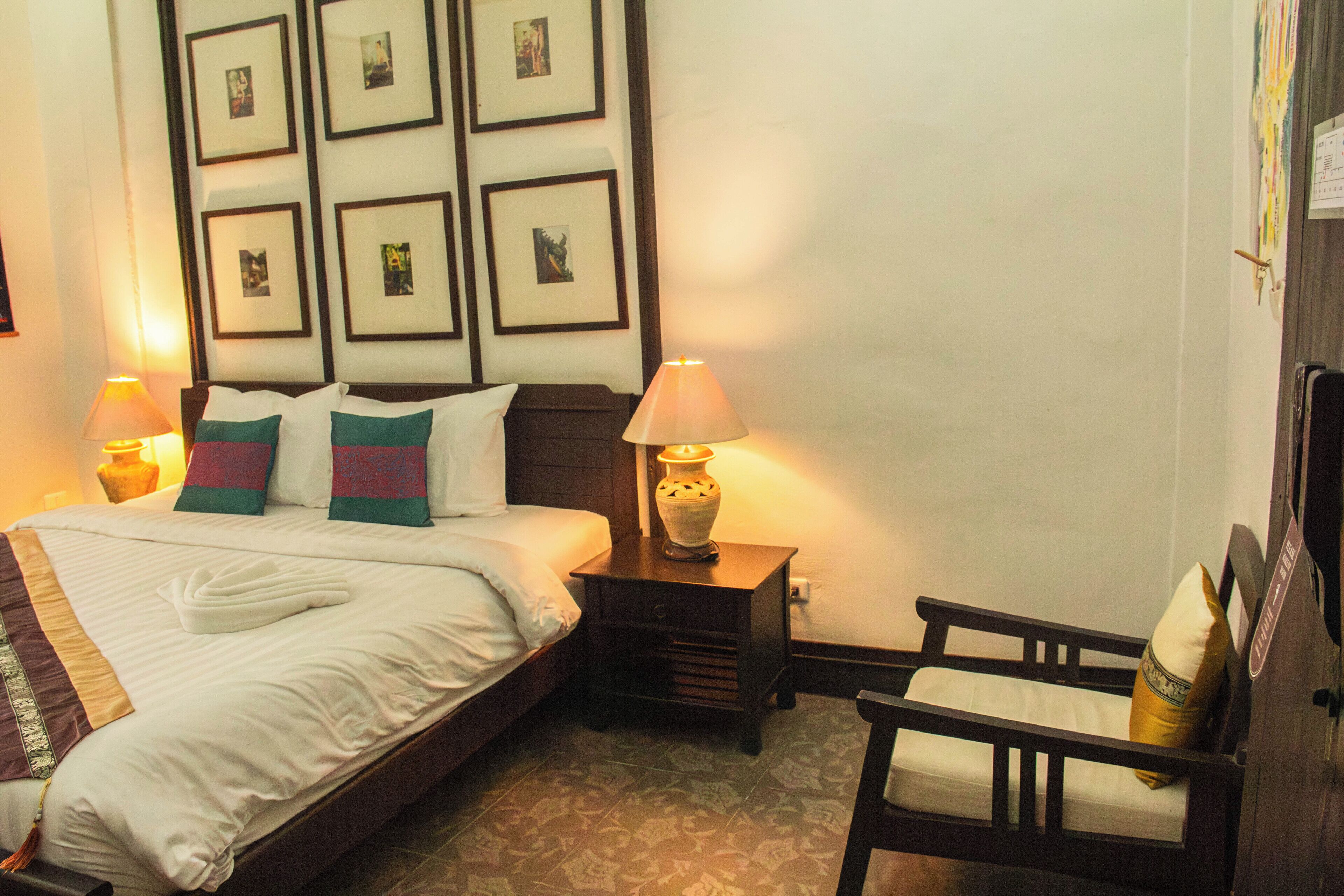 A hotel room with a bed, two bedside lamps, a chair, and a wall with framed pictures.