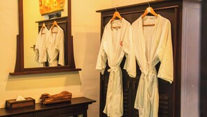 A room with a wooden cabinet holding white robes and a mirror reflecting the room. - Sunday Rainforest Chiangmai Hotel  (Chiang Mai)