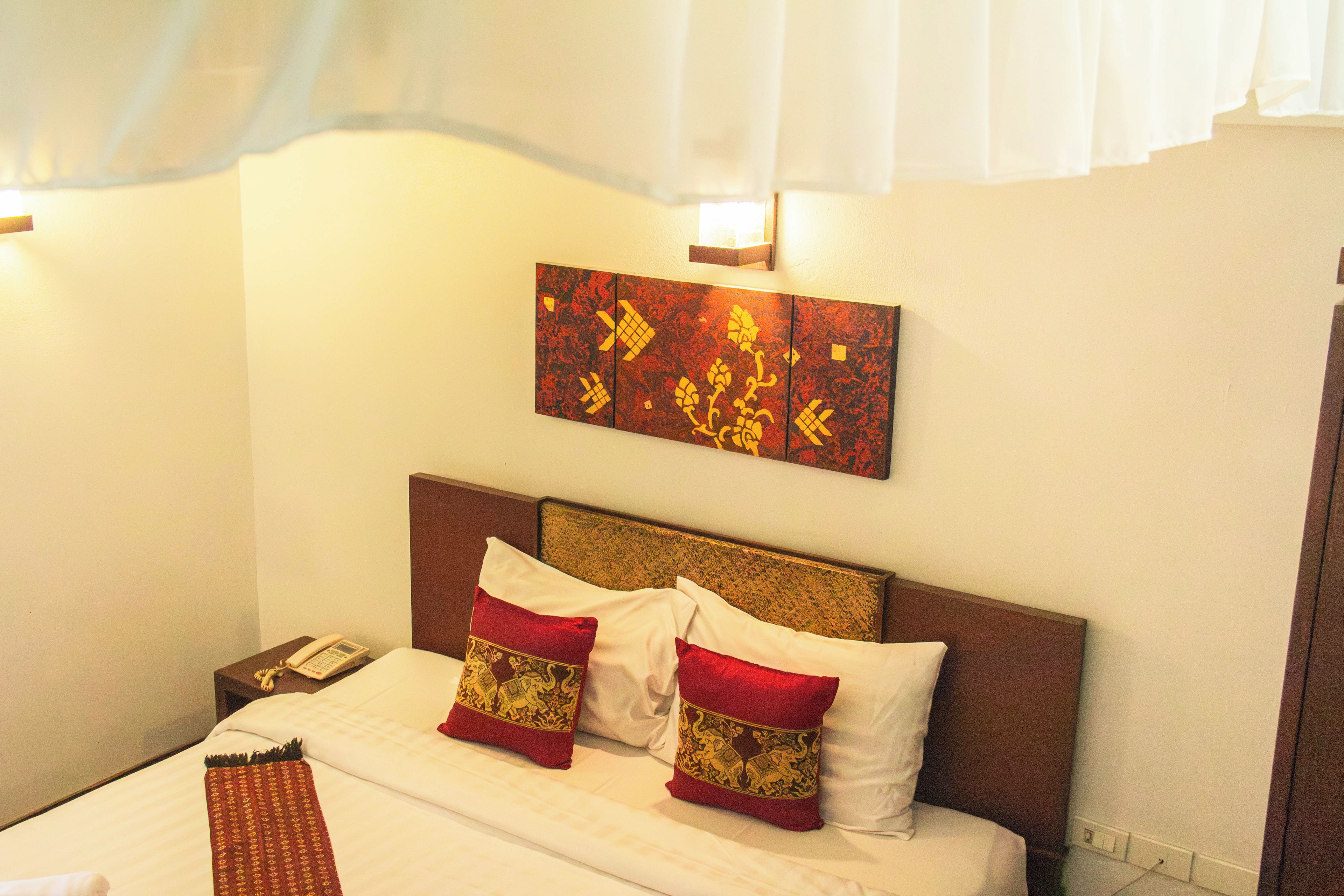 A hotel room with a bed, pillows, a nightstand with a phone, and a wall-mounted artwork.