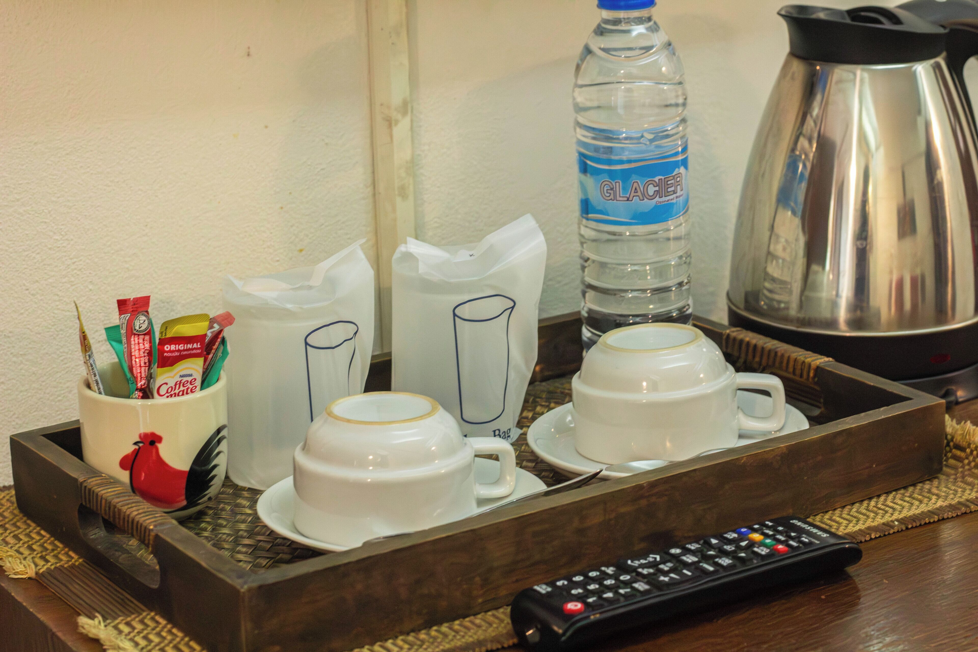A tray with coffee mugs, a water bottle, a coffee pot, and a remote control.