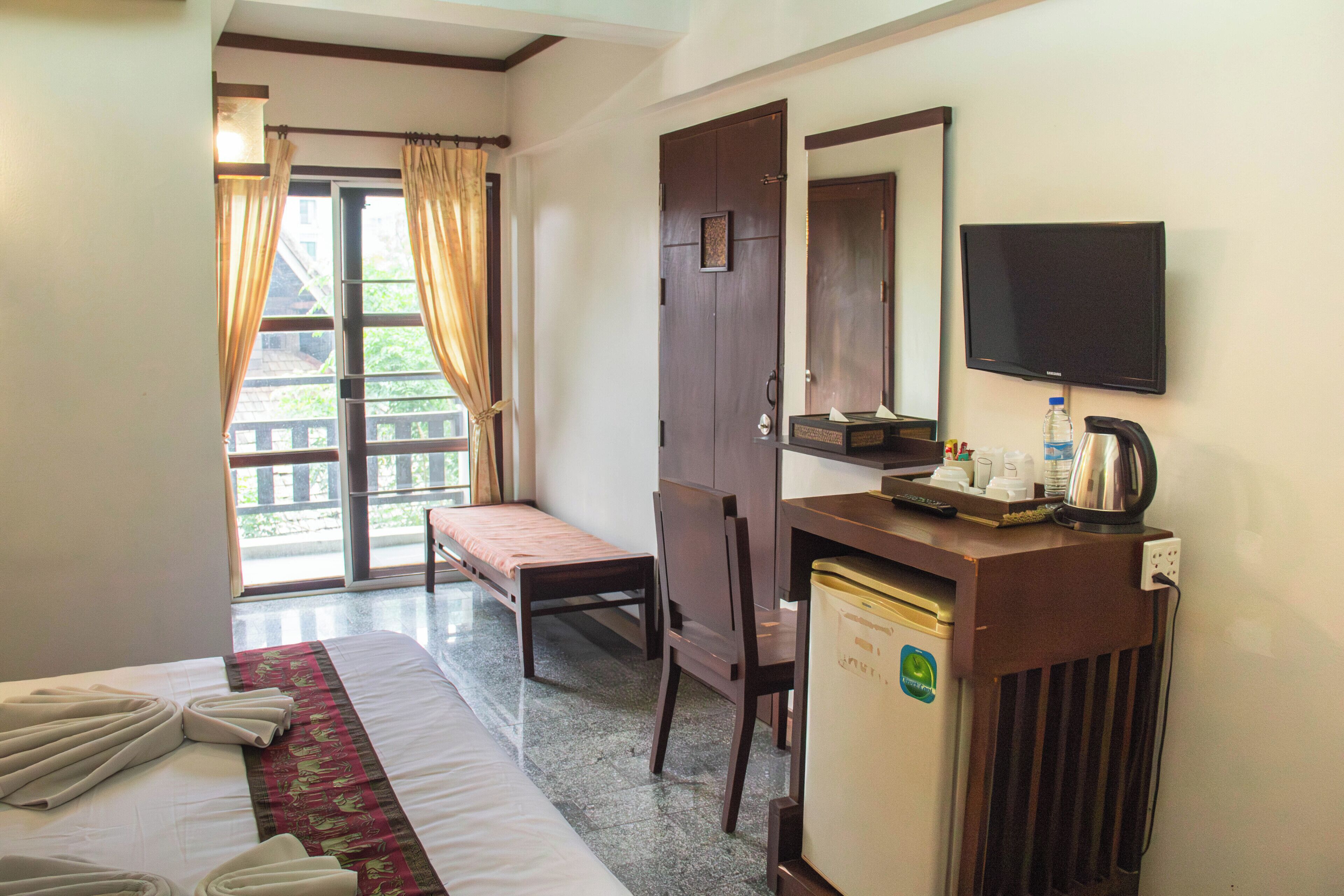 A hotel room with a bed, a desk, a chair, a television, and a window with curtains.