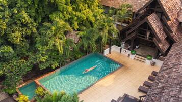 A swimming pool surrounded by lush greenery, with a wooden deck and lounge chairs.