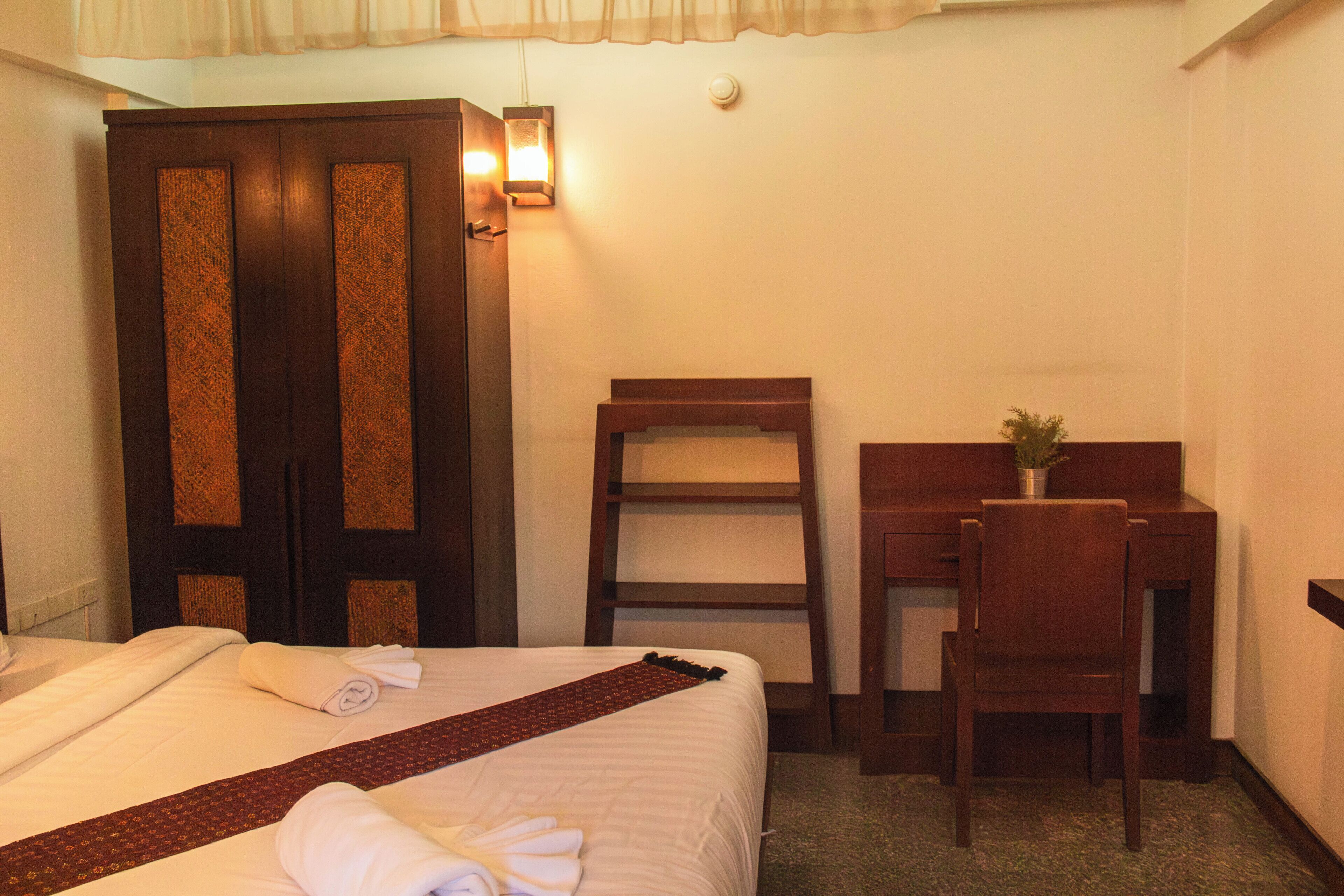 Une chambre d’hôtel avec un lit, un bureau, une chaise, une armoire et une petite plante sur le bureau.