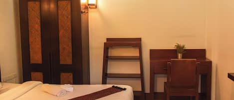A hotel room with a bed, a desk, a chair, a wardrobe, and a small plant on the desk.