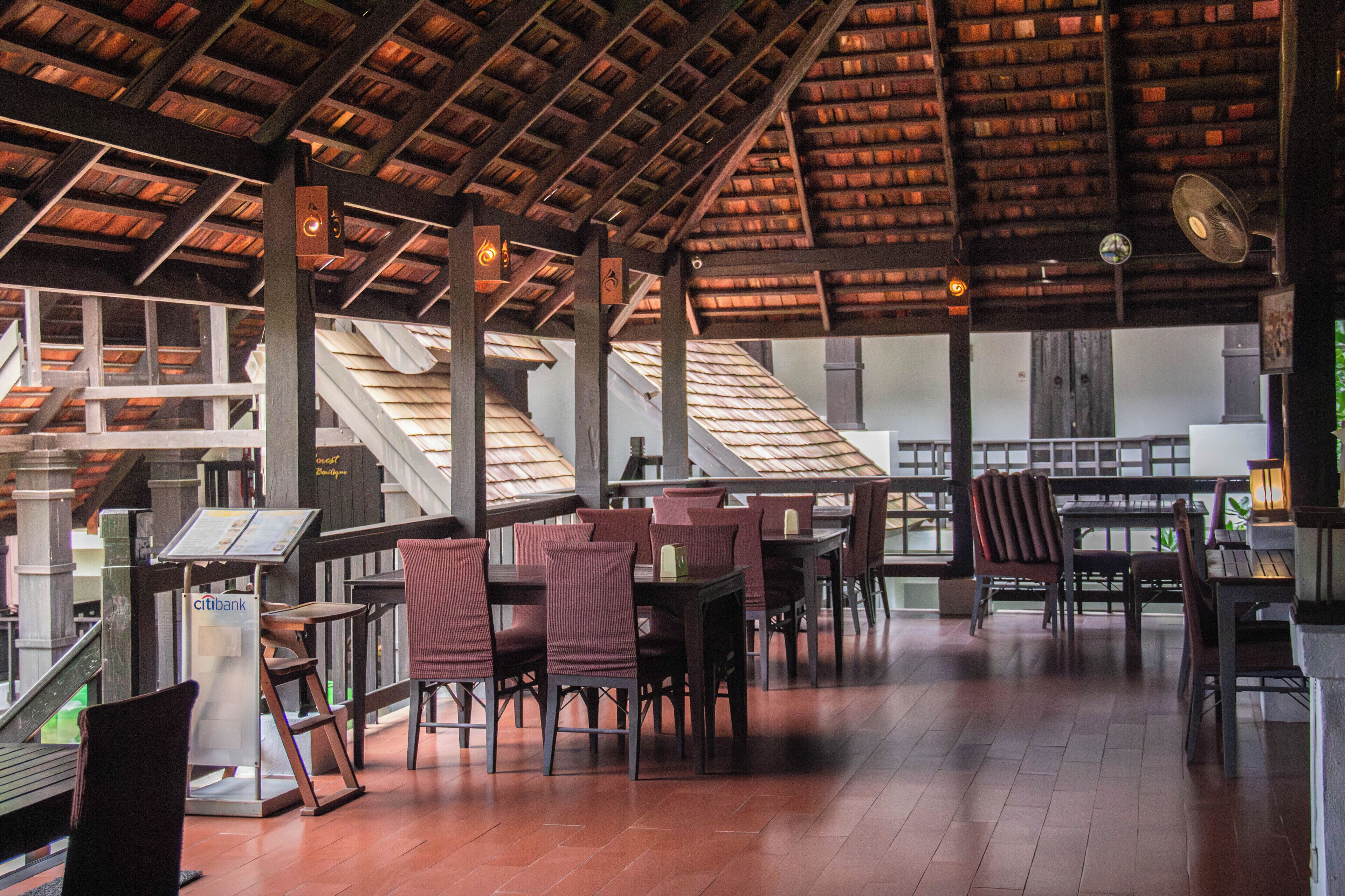 A covered outdoor seating area with tables and chairs, a staircase, and a view of the interior.