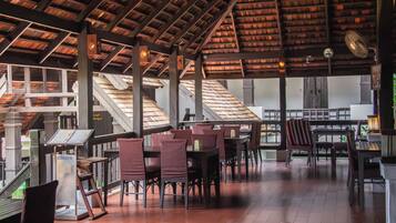 A covered outdoor seating area with tables and chairs, a staircase, and a view of the interior.