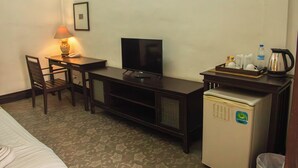 A hotel room with a bed, a desk with a television, a chair, a small refrigerator, and a tray with a kettle and cups. - Sunday Rainforest Chiangmai Hotel  (Chiang Mai)