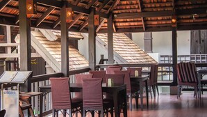 An indoor dining area with wooden tables and chairs, a high ceiling with wooden beams, and a staircase in the background. - Sunday Rainforest Chiangmai Hotel  (Chiang Mai)