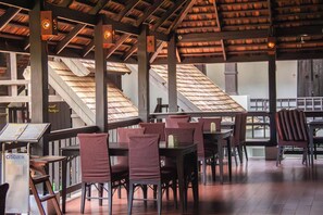An indoor dining area with wooden tables and chairs, a high ceiling with wooden beams, and a staircase in the background. - Sunday Rainforest Chiangmai Hotel  (Chiang Mai)