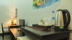 A hotel room with a desk, a lamp, a painting on the wall, a water bottle, a kettle, and a remote control. - Sunday Rainforest Chiangmai Hotel  (Chiang Mai)