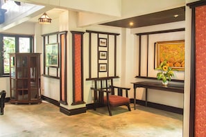Quarto com cadeira de madeira, uma mesa e um armário. Quadros emoldurados na parede e uma planta sobre a mesa.
